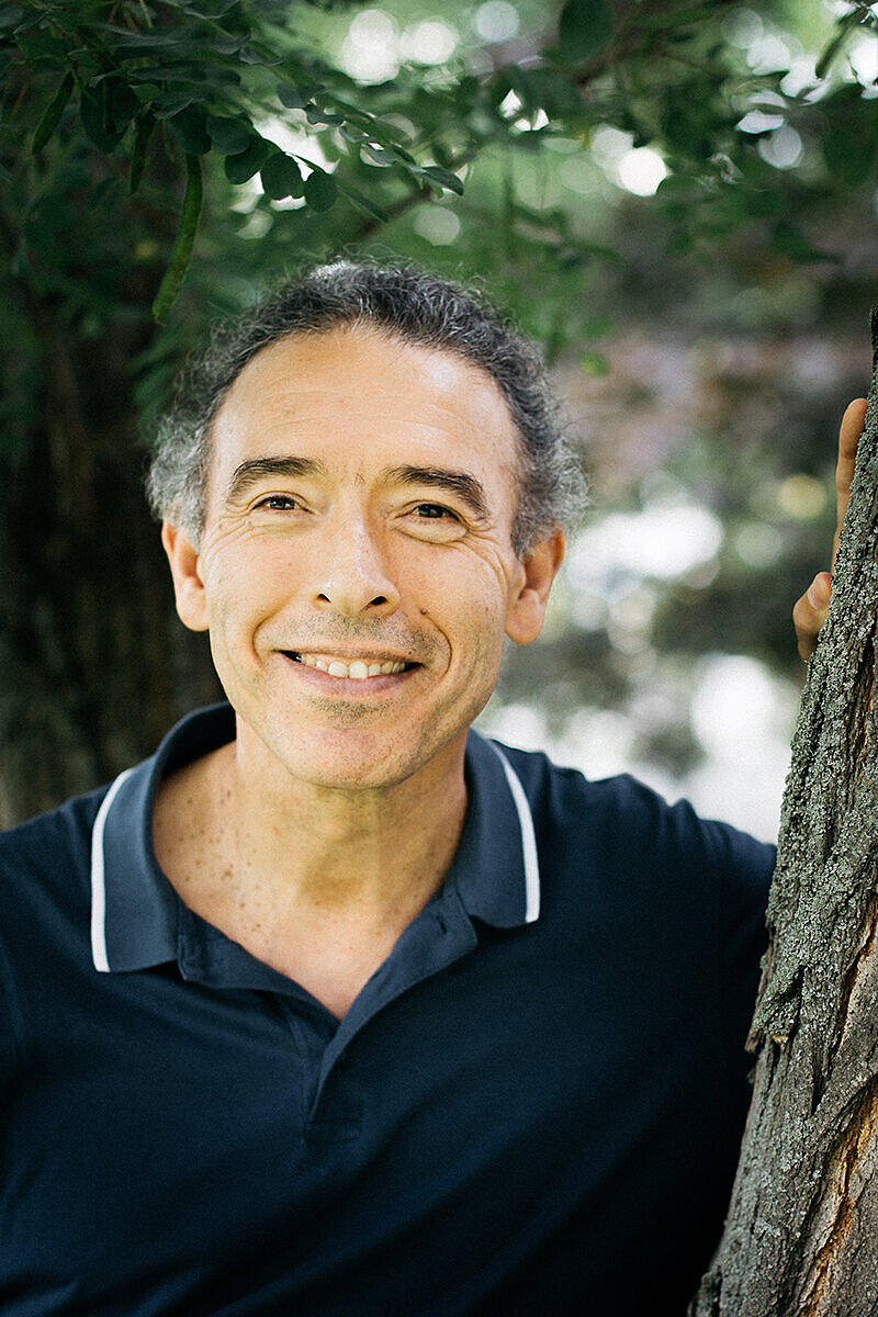 Lehrkraft Marco Pena vor grünem natürlichen Hintergrund lächelt in die Kamera