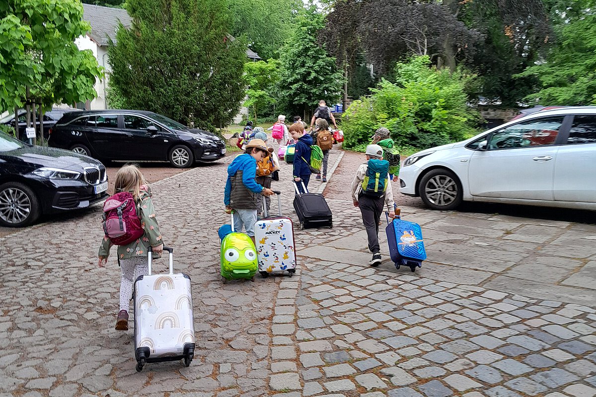 Kinder ziehen ihre Rollkoffer eine Straße entlang