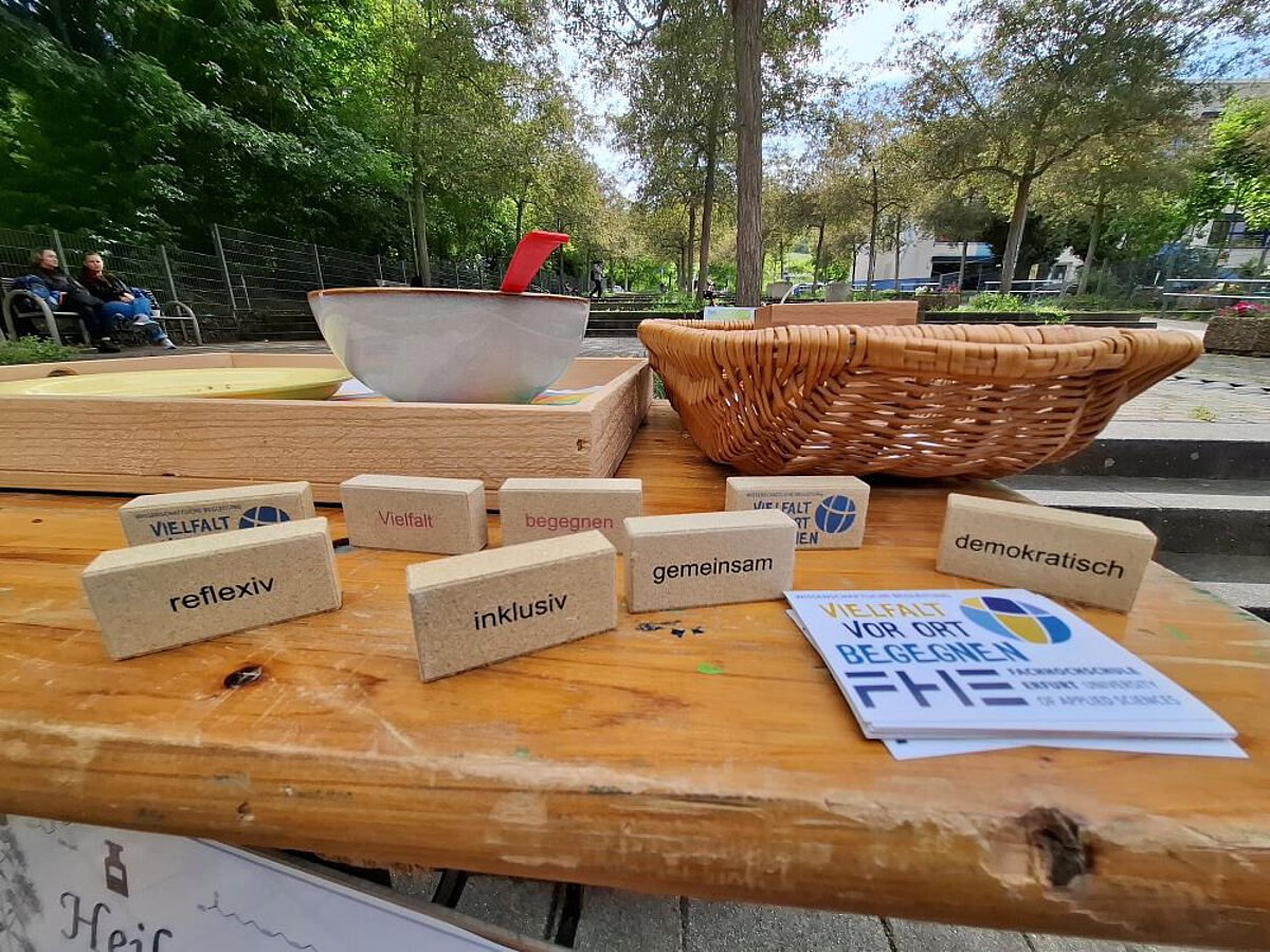 Holzbausteine mit Begriffen wie inklusiv, gemeinsam und demokratisch liegen auf einem Tisch, daneben Flyer des Projekts ‚Vielfalt vor Ort begegnen.