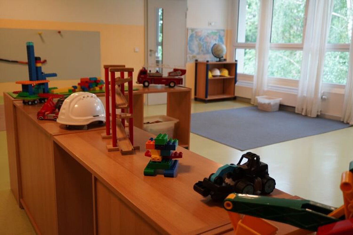 Bauraum im Kindergarten mit Bauklötzen, Spielzeugfahrzeugen, Werkbankelementen und niedrigen Regalen zum Konstruieren und Spielen.