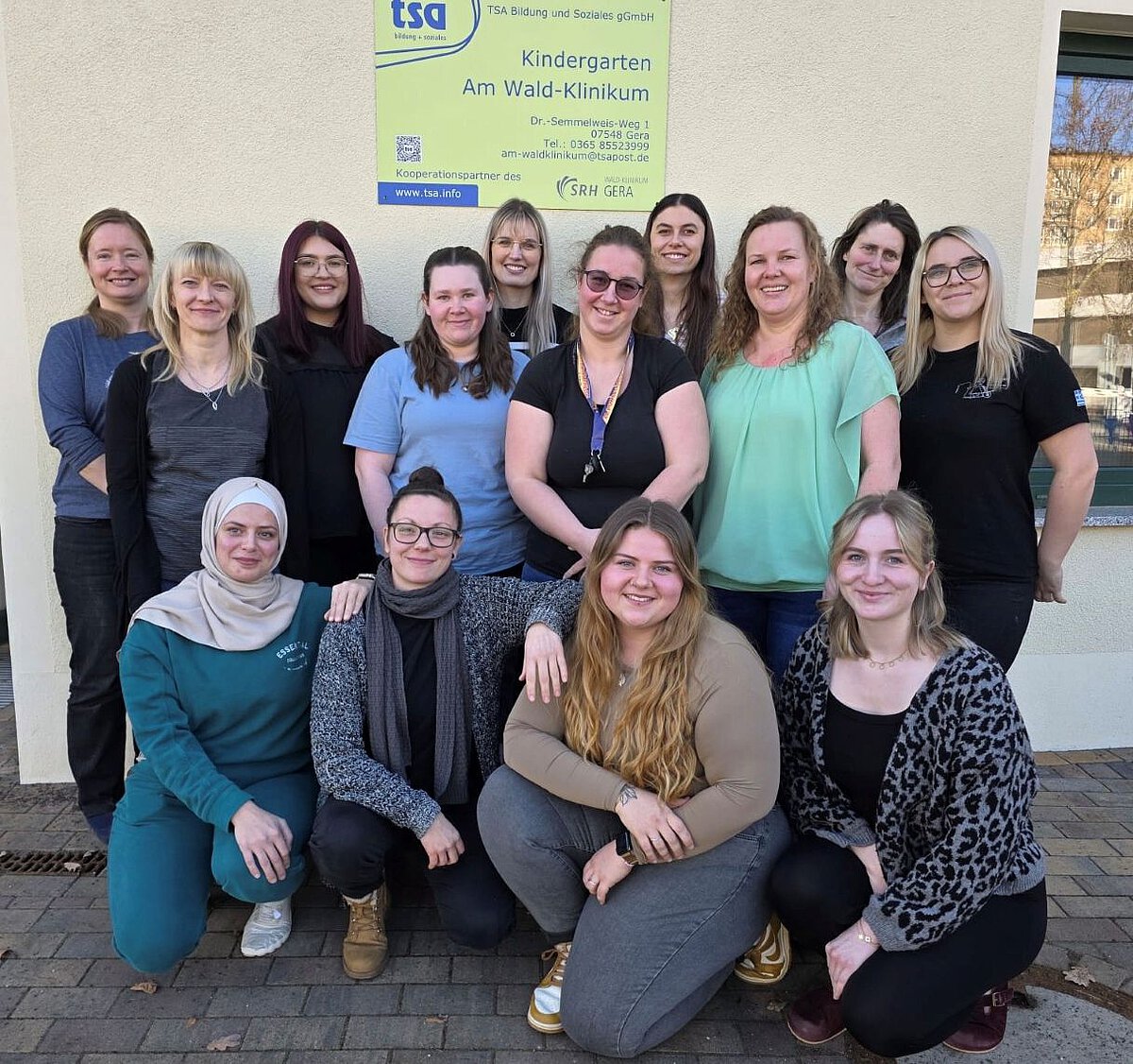 Gruppenfoto des Teams des Kindergartens „Am Wald-Klinikum“ vor dem Gebäude unter dem Einrichtungsschild.