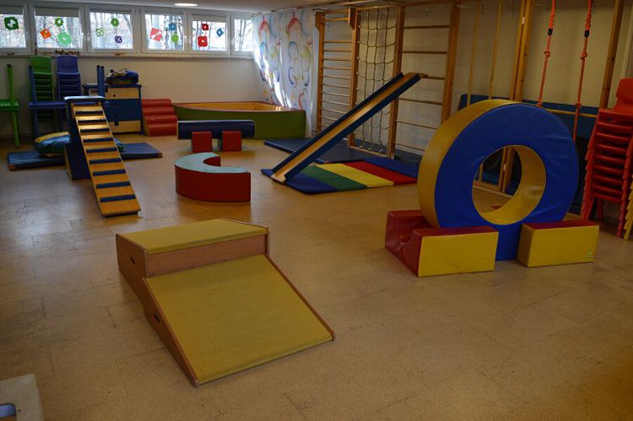 Bewegungsraum im Kindergarten mit Turn- und Spielelementen wie Matten, Kletter- und Balanciergeräten sowie großen Schaumstoffmodulen.