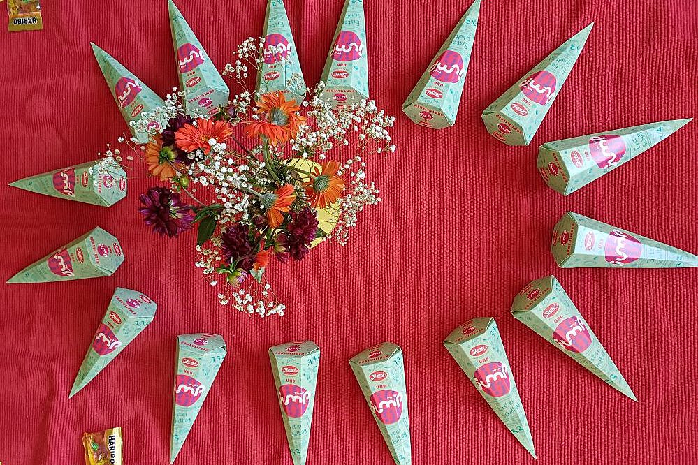 Zuckertüten in Kreisform auf rotem Tuch mit Blumen in der Mitte.