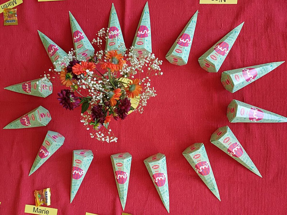 Zuckertüten in Kreisform auf rotem Tuch mit Blumen in der Mitte.