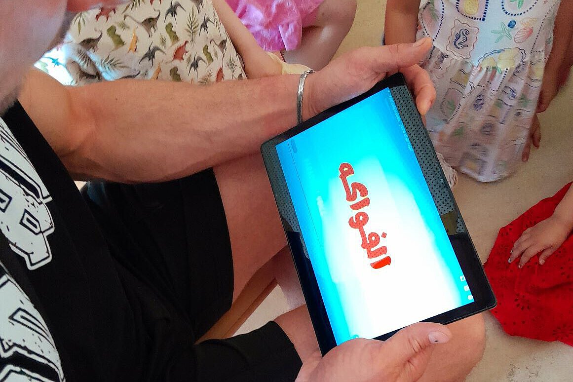 Pädagogische Fachkraft zeigt Kindern ein Tablet mit digitalem Inhalt im Kita-Alltag