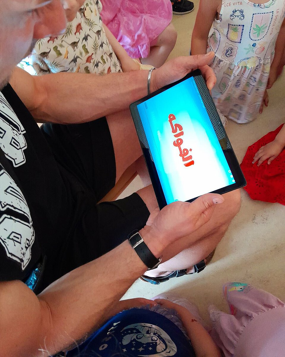 Pädagogische Fachkraft zeigt Kindern ein Tablet mit digitalem Inhalt im Kita-Alltag
