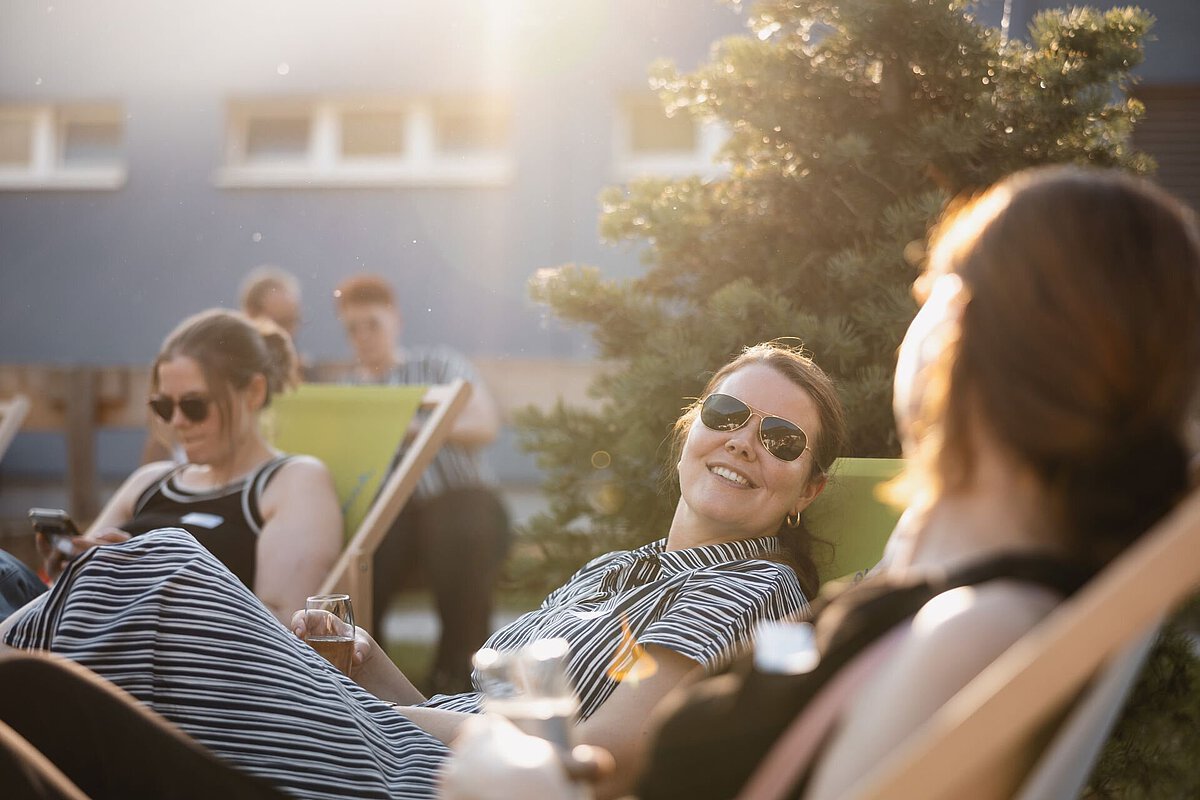 Mehrere Personen sitzen entspannt auf Liegestühlen im Außenbereich und genießen eine Veranstaltung in der Abendsonne.