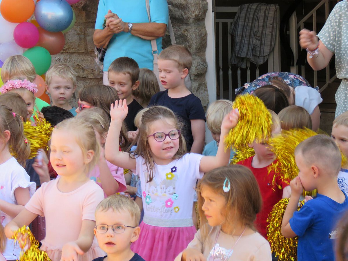 Kinderfest - Kindergarten Windischholzhausen - Fröhliche Kinder Zwischen vielen Kindern steht ein Mädchen, dass fröhlich die Hände nach oben steckt und tanzt