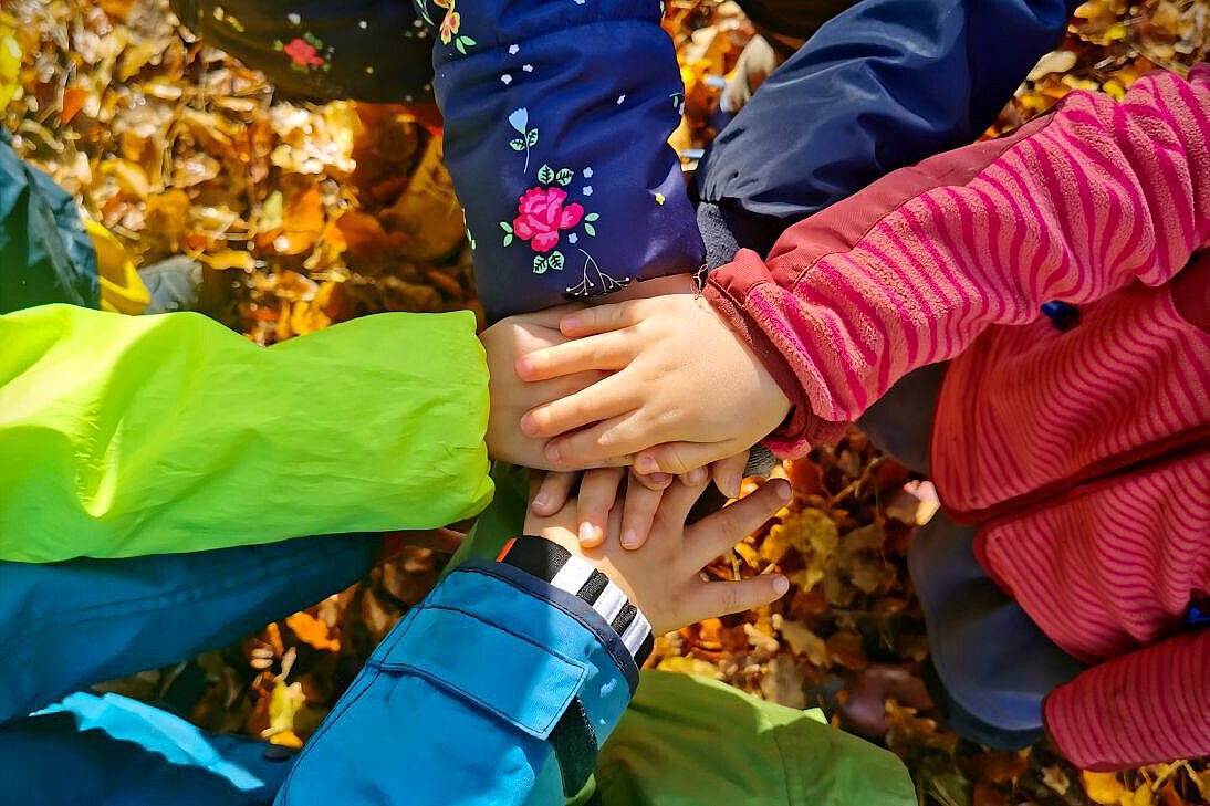 Kinder des Kindergarten Burgweg legen die Hände übereinander, man sieht nur die Arme in bunten Jacken