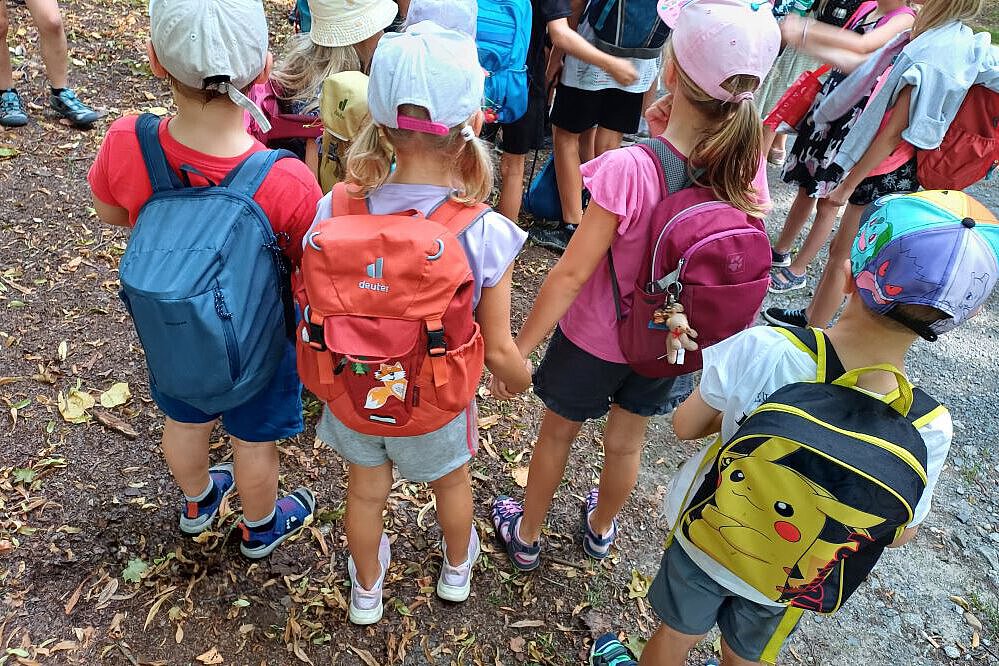 Gruppe von Kindern mit bunten Rucksäcken steht auf einem Waldweg.