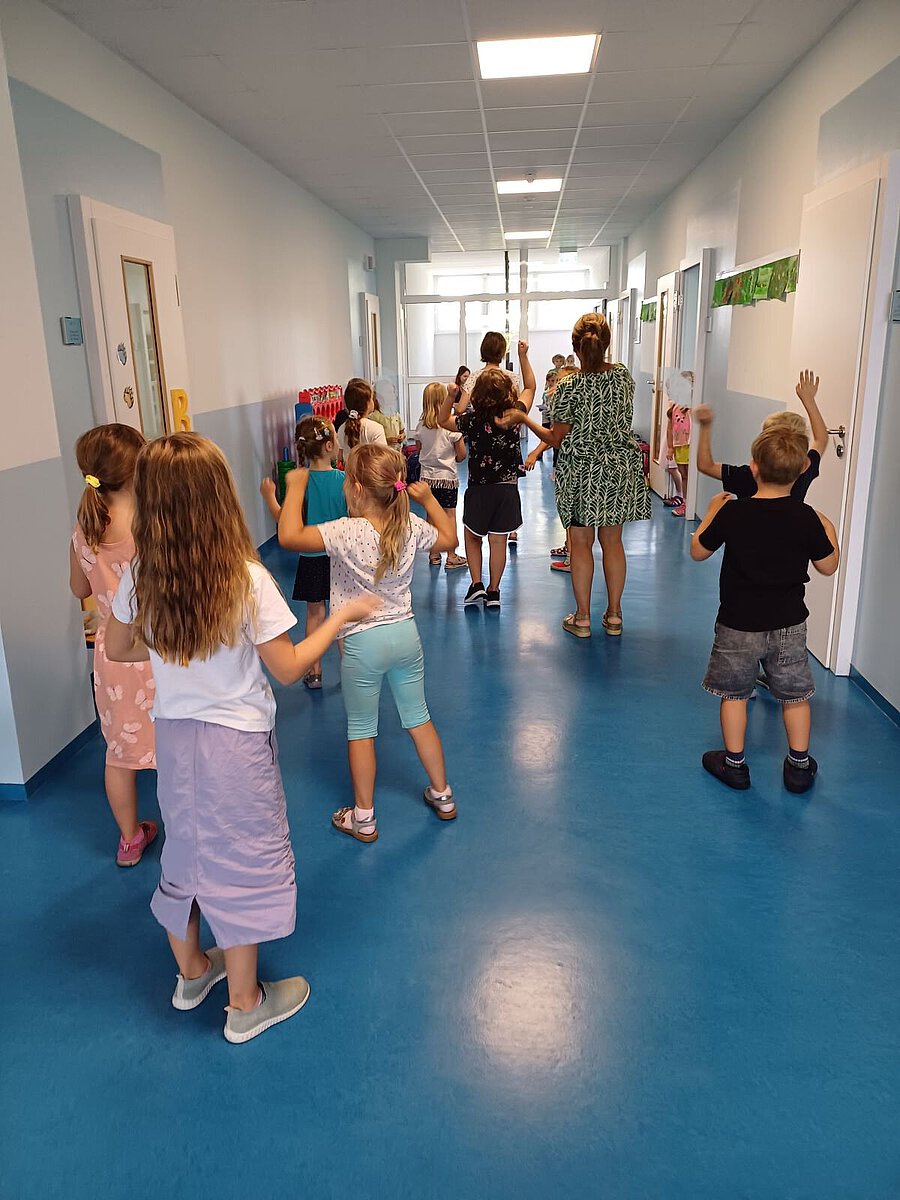 Gruppe von Kindern und eine Betreuungsperson gehen durch einen hellen Flur.