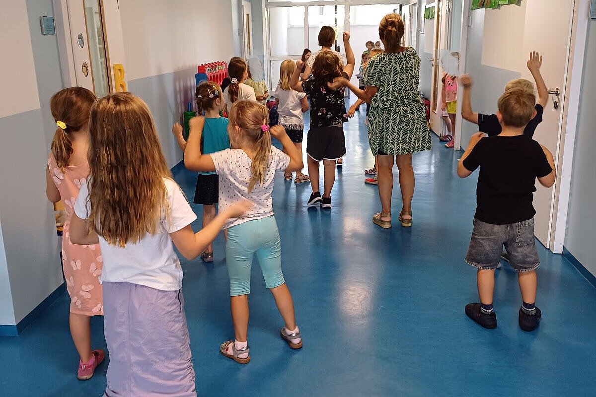 Gruppe von Kindern und eine Betreuungsperson gehen durch einen hellen Flur.