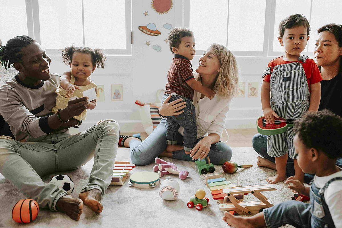 Erzieher und Erzieherinnen spielen im Kreis sitzend mit den Kindern