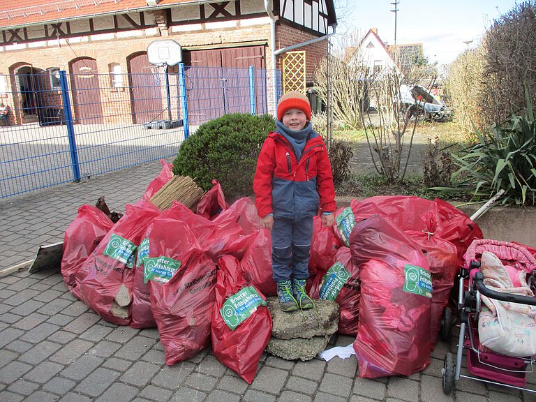 Müllsammelaktion - Umweltbewusstsein - Kindergarten Windischholzhausen Ein Kind steht vor vielen roten Müllsäcken, die von Eltern und Kindern gefüllt wurden, um an unserer Müllsammelaktion teilzunehmen