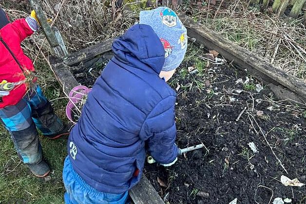 Kinder arbeiten im Gartenbeet und lockern gemeinsam die Erde mit kleinen Werkzeugen.