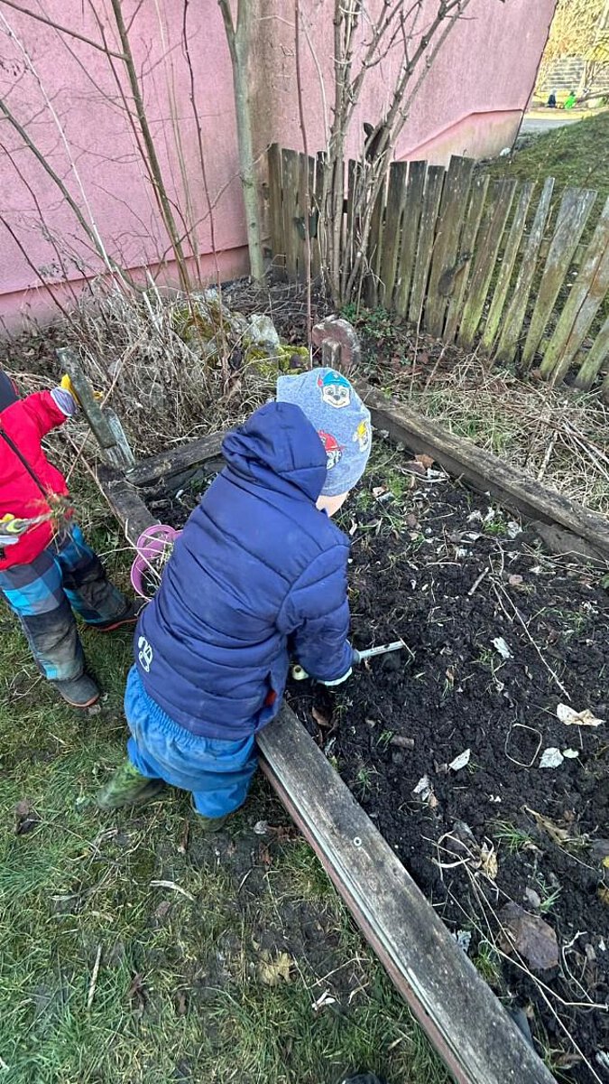 Kinder arbeiten im Gartenbeet und lockern gemeinsam die Erde mit kleinen Werkzeugen.