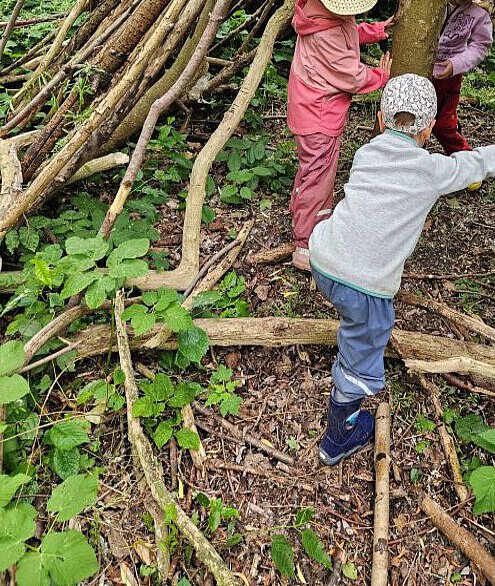 Kinder entdecken den Wald und bauen mit gesammelten Ästen ein kleines Naturversteck.