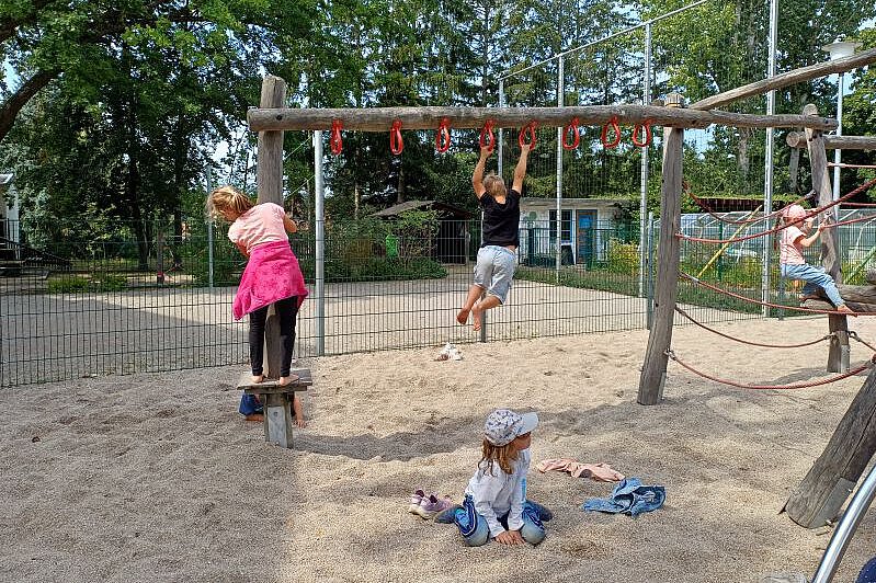Kinder spielen auf einem Holz-Klettergerüst im Sandbereich.