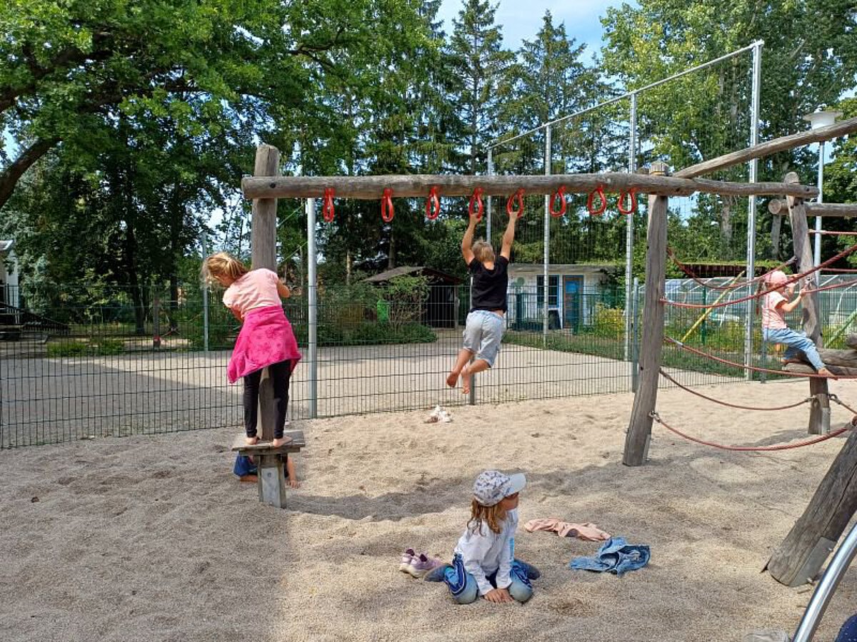 Kinder spielen auf einem Holz-Klettergerüst im Sandbereich.
