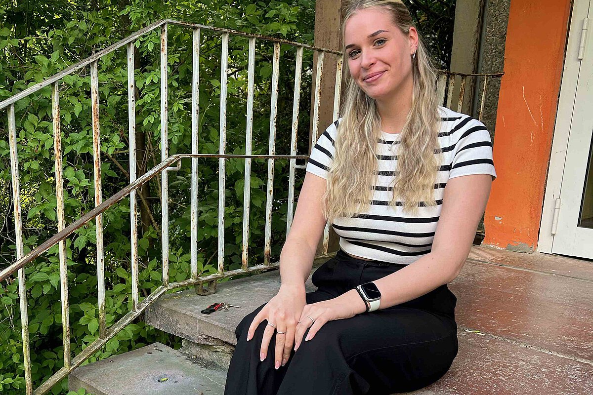 Interviewpartnerin Antonia Kühne sitzt auf der Treppe vor dem Eingang der Sozialen Dienste der TSA