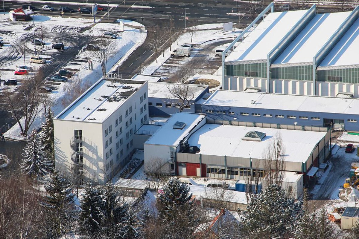 Luftaufnahme des Akademiehotels Jena im Winter mit verschneiten Dächern, umliegenden Gebäuden und Parkplätzen