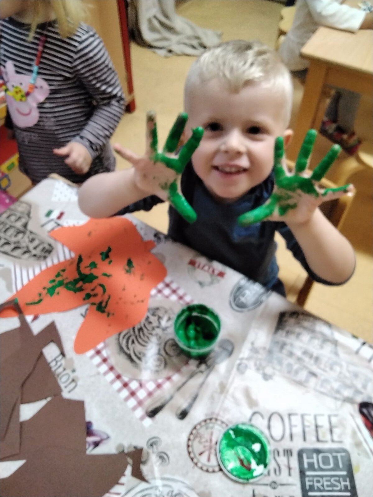 Kreative Kunst - Fingerfarben - Spaß - Kindergarten Windischholzhausen Ein Junge sitzt am Maltisch und zeigt seine grün bemalten Finger