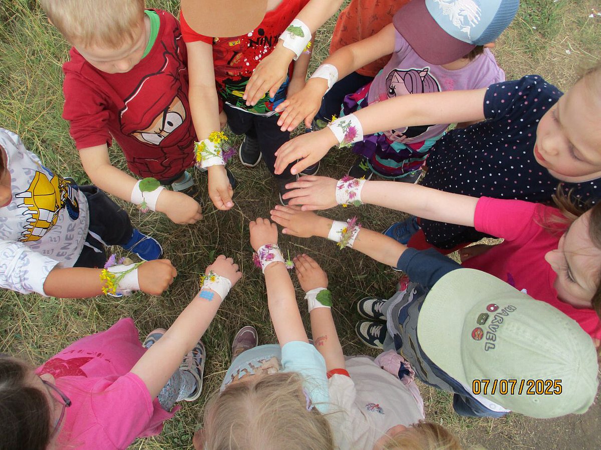 Zusammenhalt - Gemeinschaft - Freundschaft - Kindergarten Windischholzhausen Elf Kinder zeigen ihre Naturarmbänder. Kreppband wurde um ihr handgelenk gewickelt und darauf befestigten sie Naturmaterialien wie z.B. Blüten, Blätter oder Gräser die sie in ihrer Umgebung fanden