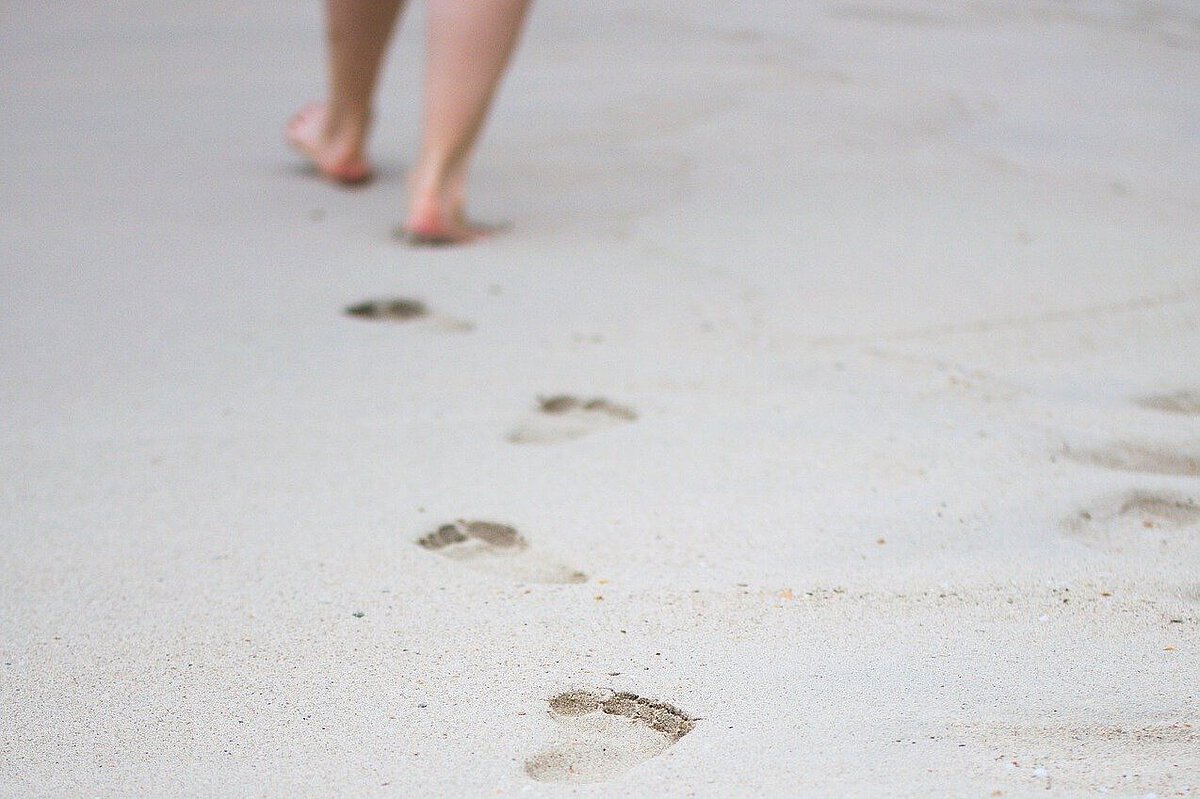 Person hinterlässt Fußspuren im Sand und entfernt sich aus dem Bild.