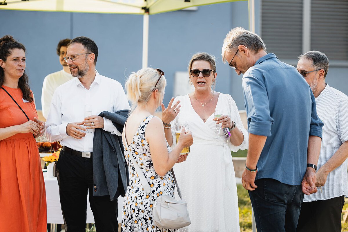 Netzwerken und Austausch unter Gästen bei Event Mehrere Personen stehen im Außenbereich zusammen, unterhalten sich und halten Getränke während einer Veranstaltung.