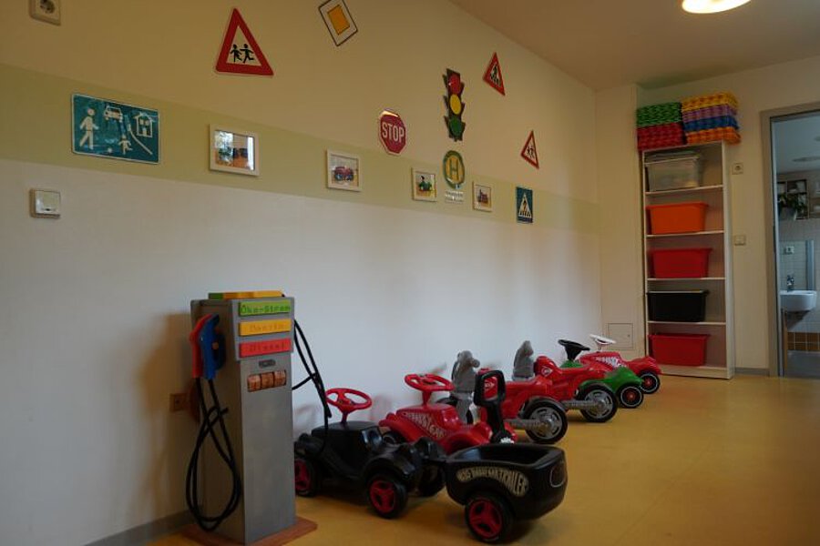 Flurbereich in der Krippe mit Kinderfahrzeugen, Laufautos und Spieltankstelle, Wandgestaltung mit Verkehrszeichen.