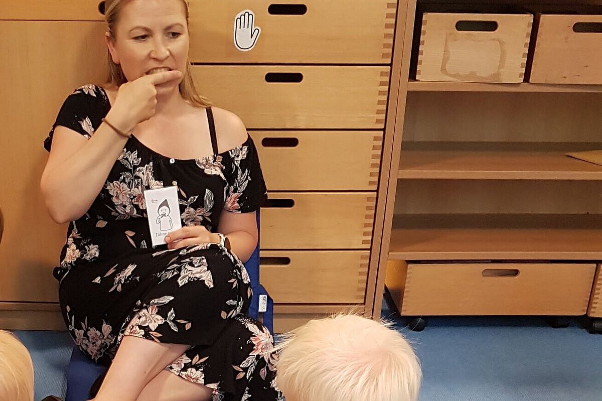 Spielerische Vermittlung von Zahnhygiene in der Kita Pädagogische Fachkraft zeigt mithilfe einer Bildkarte das Thema Zähneputzen und erläutert den Kindern die Zahnpflege.