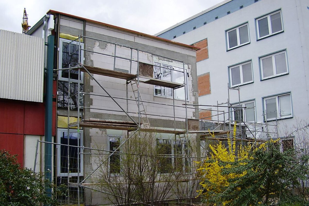 Akademiehotel Jena 2008 – Umbau Verbindungsbau Umbau des Verbindungsbaus am Akademiehotel mit Gerüst, freigelegter Fassade und Baustelle im Außenbereich mit Sträuchern und gelb blühender Pflanze