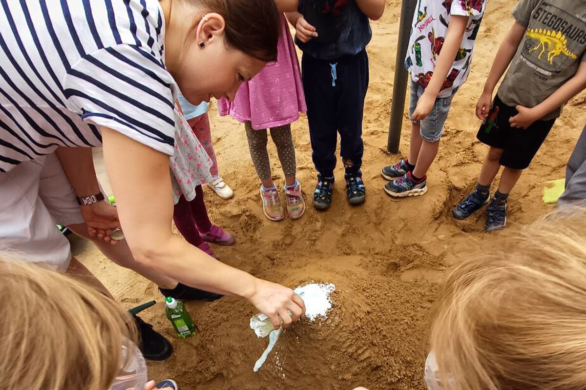 Kinder beobachten gemeinsam mit einer pädagogischen Fachkraft ein Experiment im Außengelände der Kita Bergfelderweg.