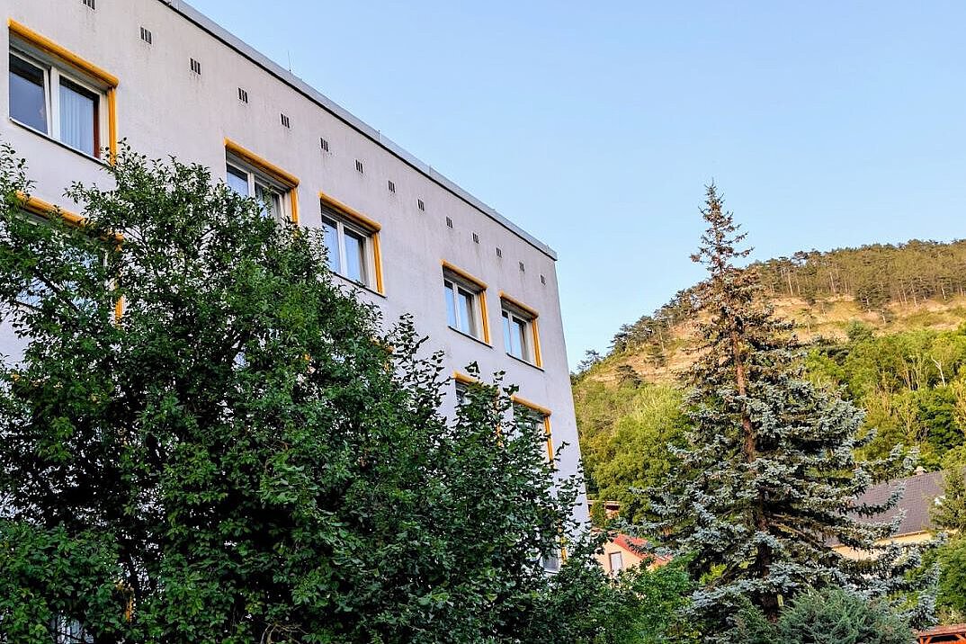 Akademiehotel Jena – Außenansicht 2025 Modernisierte Außenansicht des Akademiehotels mit heller Fassade, gelben Fensterrahmen und umgebender Begrünung vor bewaldetem Hang