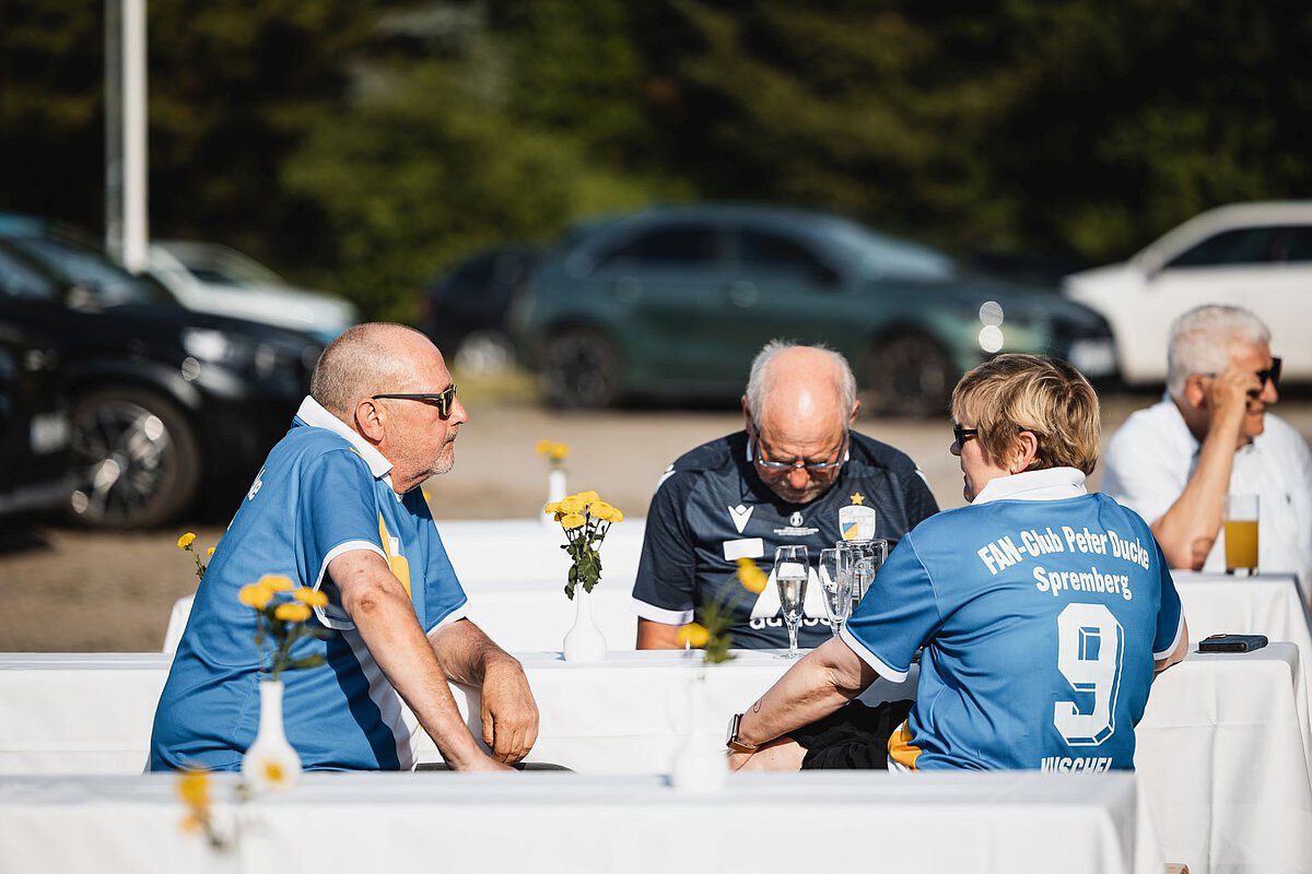 Stammgäste des Akademiehotels beim entspannten Austausch im Außenbereich Mehrere Personen sitzen an Tischen im Außenbereich, unterhalten sich und genießen Getränke während einer Veranstaltung.
