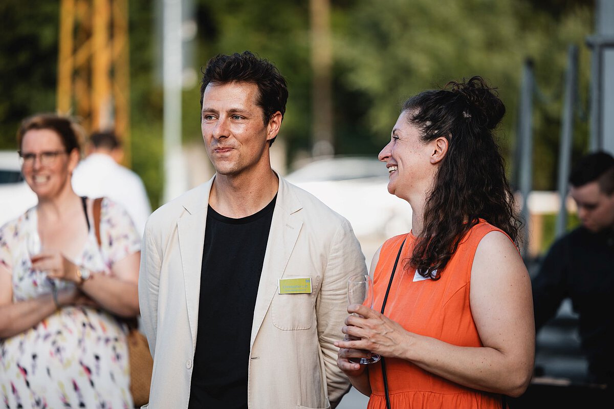 Austausch und Networking bei Veranstaltung im Außenbereich Mehrere Personen stehen im Freien zusammen, unterhalten sich und halten Getränke bei einer Veranstaltung.