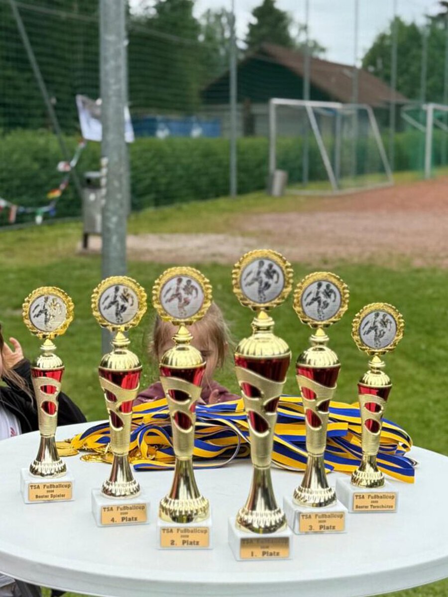 Pokale und Medaillen des TSA Fußball-Cups 2026 auf einem Tisch auf dem Sportplatz in Vieselbach