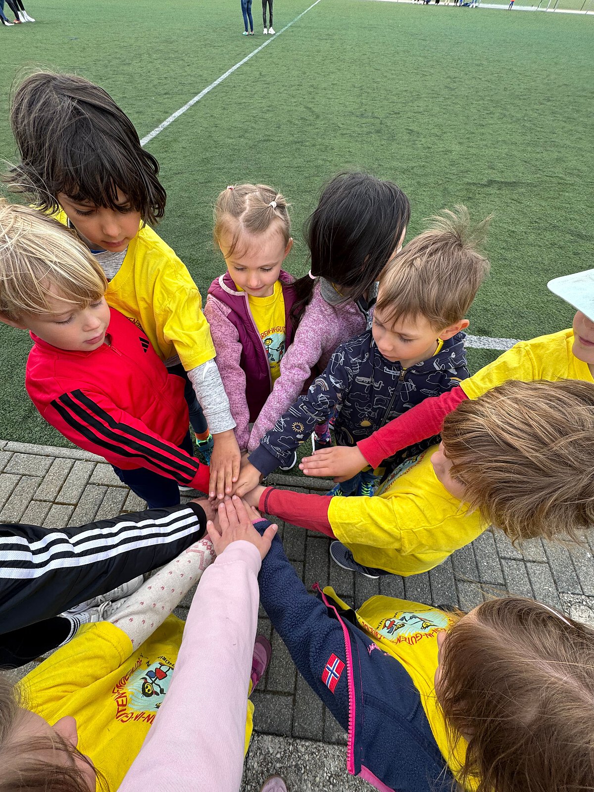 Kinder und Schüler legen im Kreis die Hände übereinander, Teamgeist