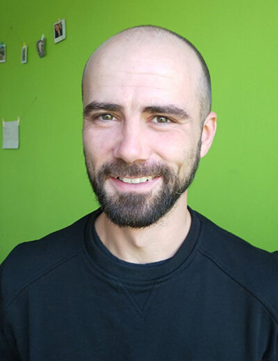 Lehrkraft Philipp Bräunig vor grünem Hintergrund lächelt in die Kamera