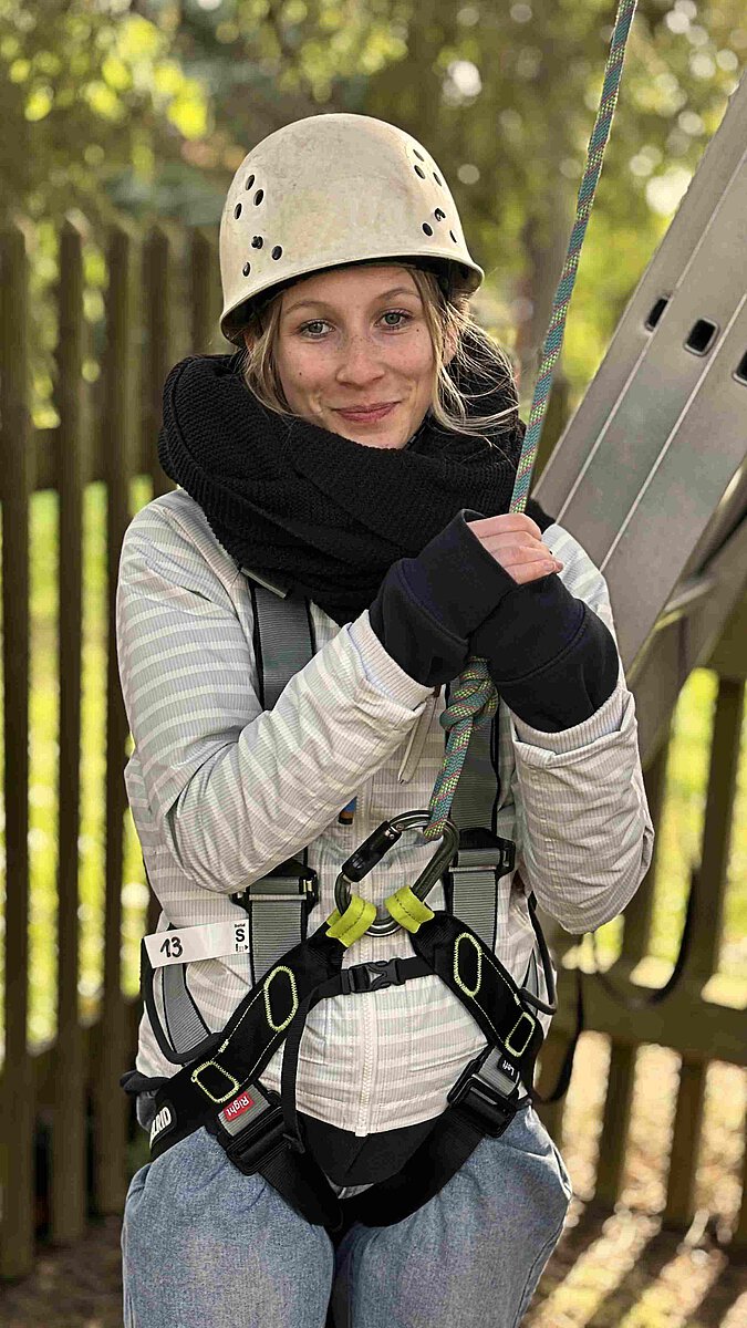 erson mit Schutzhelm und Sicherungsgurt beim Klettertraining im Außenbereich