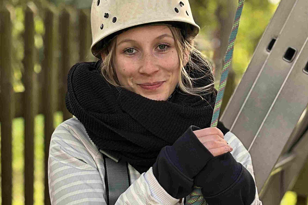 erson mit Schutzhelm und Sicherungsgurt beim Klettertraining im Außenbereich