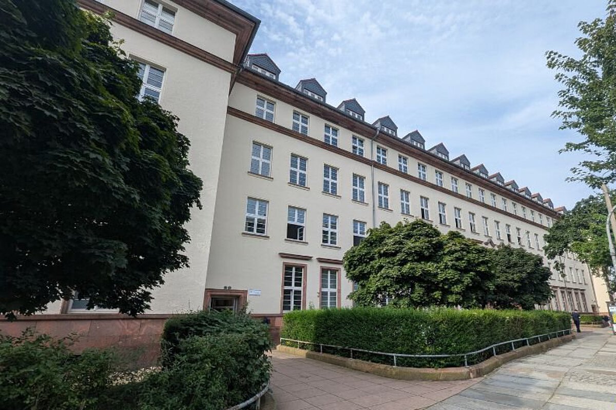 Gebäudeansicht der Freien berufsbildenden Schule Dresden mit viel Grün, zu sehen ist der Vordereingang des Gebäudes.