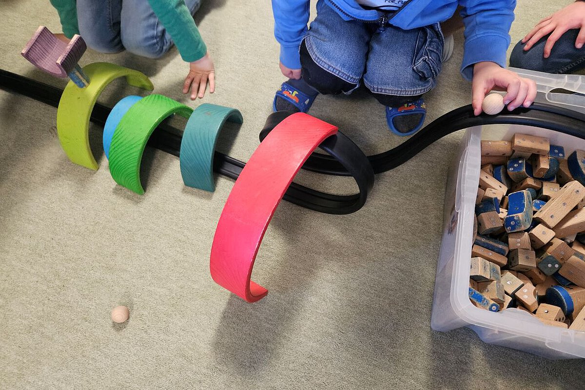 Kinder spielen mit bunten Holzelementen und bauen eine Rennbahn für Kugeln.