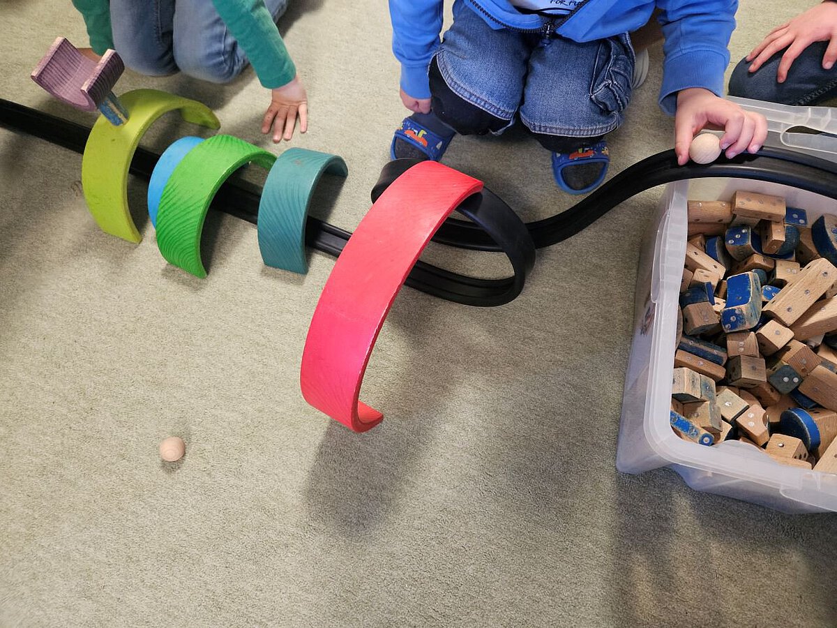 Kinder spielen mit bunten Holzelementen und bauen eine Rennbahn für Kugeln.