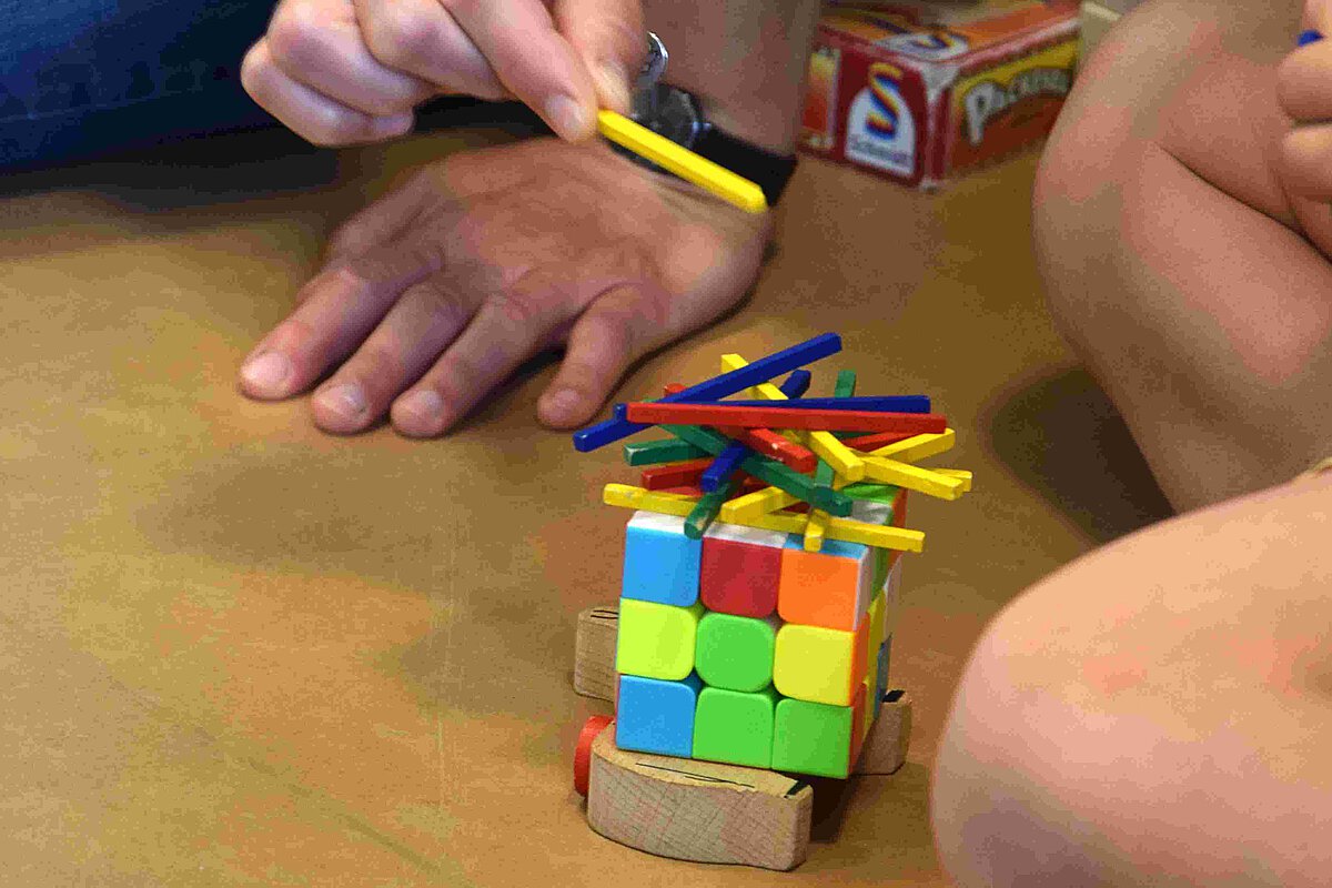 Fachliche Gedanken Ausbildung Erzieher spielt mit Kind ein Geschicklichkeitsspiel mit bunten Würfeln und Stäbchen