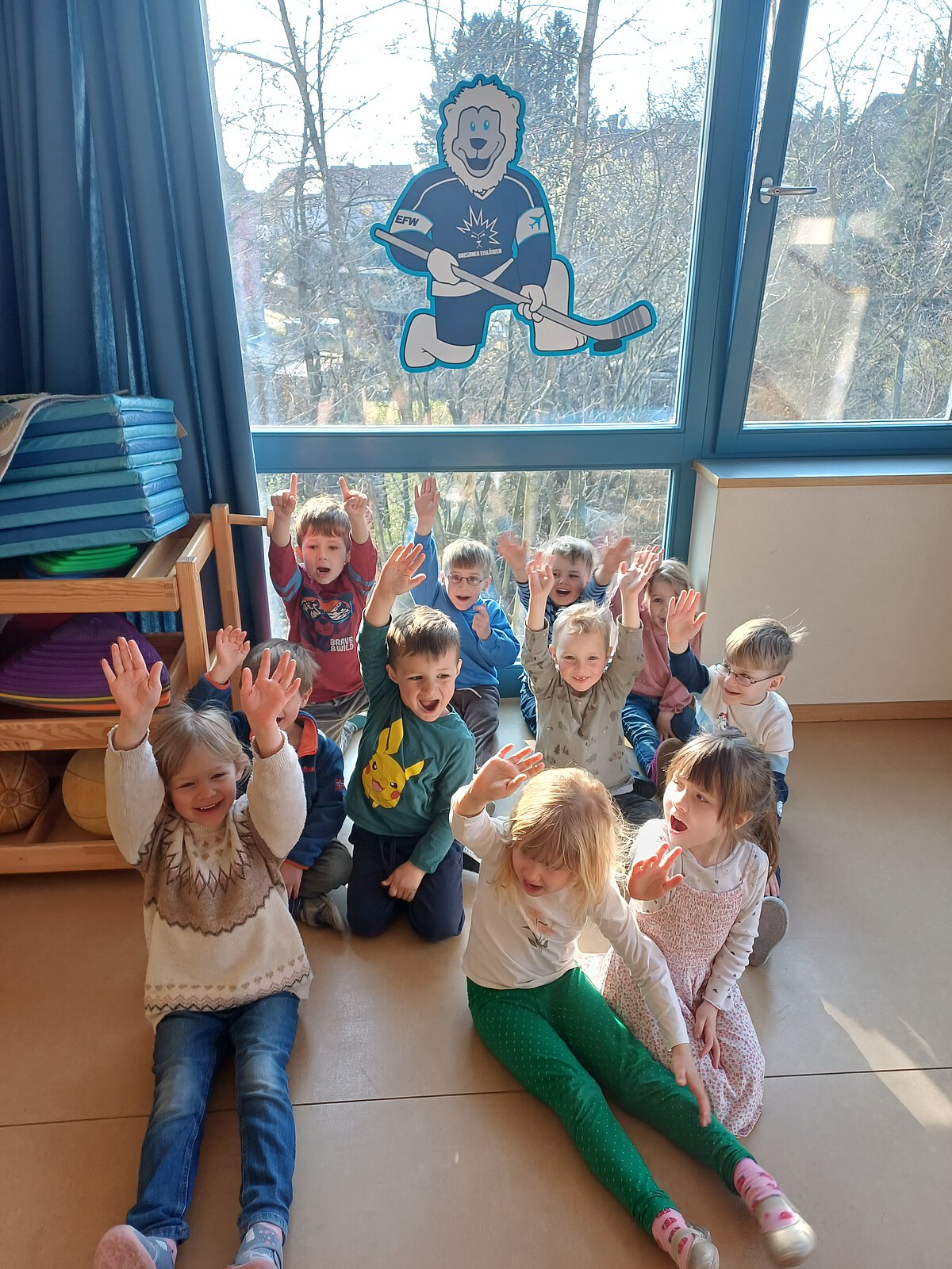 Kinder sitzen freudig im Bewegungsraum vor dem Logo des Eislöwen Kids-Club