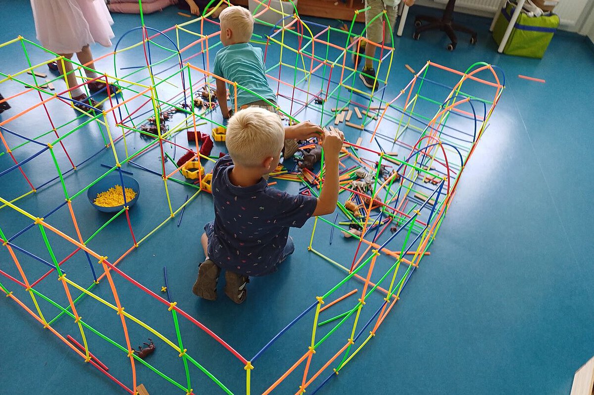 Kinder bauen mit bunten Steckstäben eine große Konstruktion auf blauem Boden.