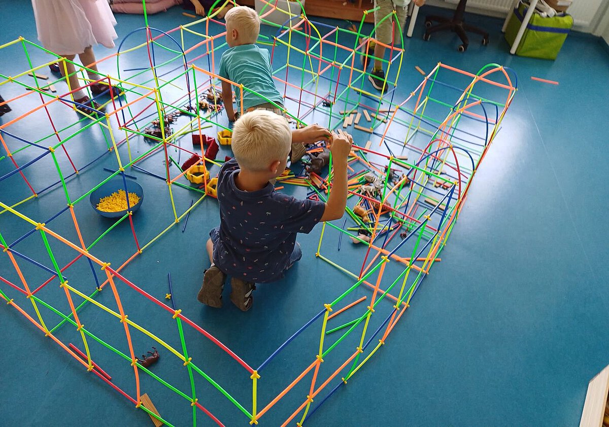 Kinder bauen mit bunten Steckstäben eine große Konstruktion auf blauem Boden.