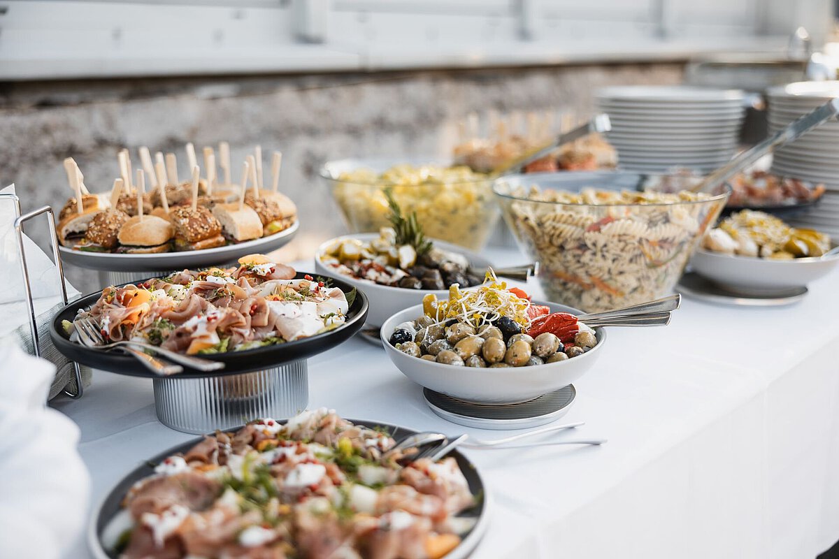 Vielfältiges Buffet mit Salaten, Fingerfood und Gegrilltem auf einem gedeckten Tisch.