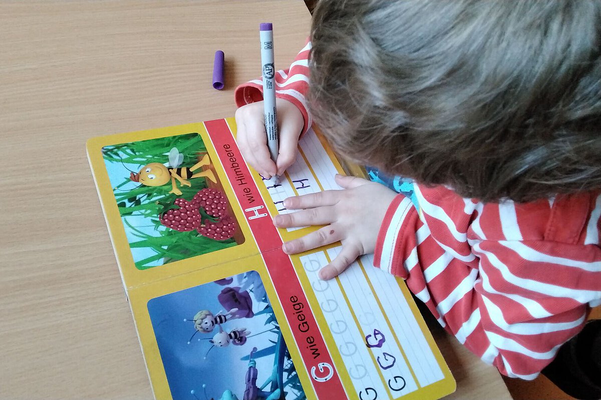 Kind schreibt Buchstaben in einem Übungsheft im Kindergarten Wogau